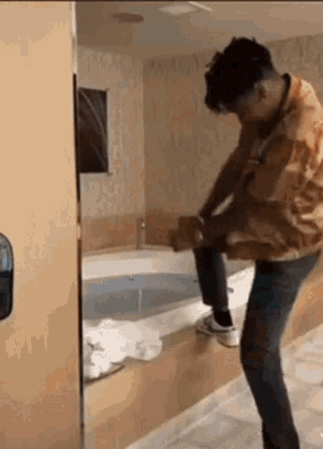 a man is standing in a bathroom next to a bathtub and taking off his pants .