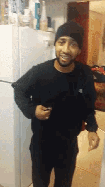 a man wearing a black champion sweatshirt stands in front of a refrigerator