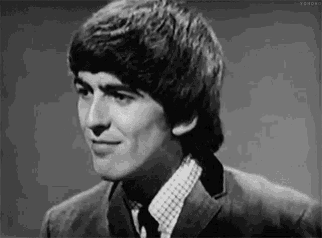a black and white photo of a young man in a suit and tie smiling .