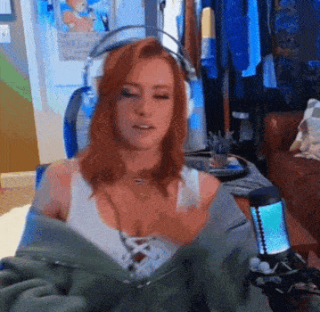 a woman with red hair is wearing headphones and a jacket while sitting in front of a microphone .