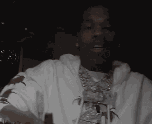 a man wearing a white hoodie and a chain around his neck looks at the camera .