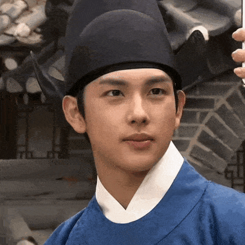 a man wearing a black hat and a blue robe looks at the camera