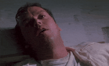 a man in a white shirt is laying down with his eyes closed