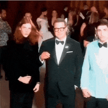 a man in a tuxedo holds hands with two other men at a party