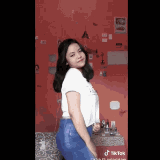 a girl in a white shirt and blue jeans is dancing in front of a red wall .