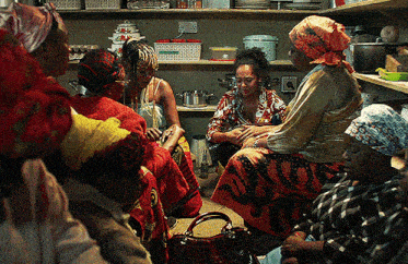 a group of women are sitting in a room with shelves full of pots and pans