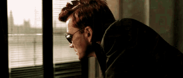 a man wearing sunglasses is looking out of a window .