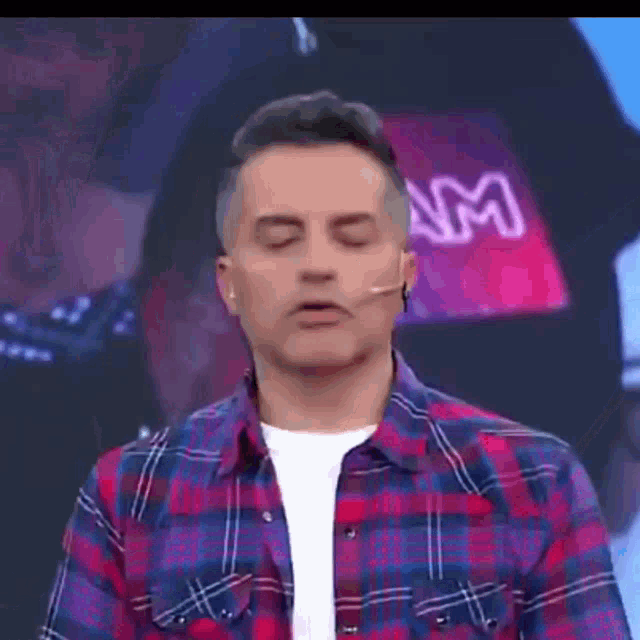 a man in a plaid shirt is standing in front of a microphone .