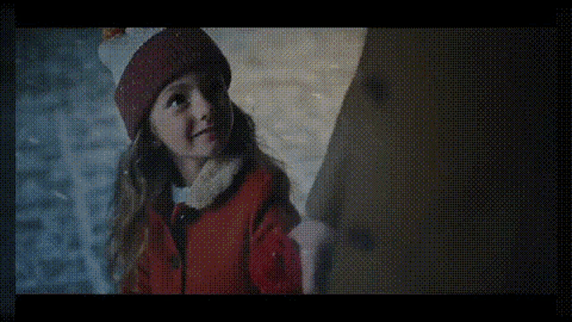 a little girl wearing a red coat and a red hat is standing in front of a snow sculpture .
