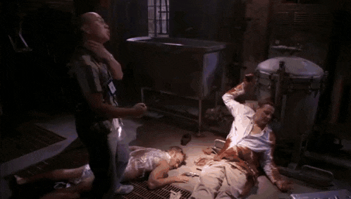 a group of people are standing around a man laying on the floor covered in blood .