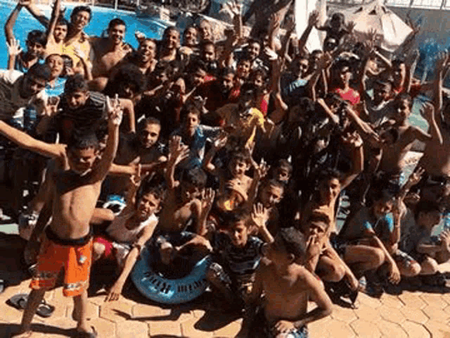a group of young people are posing for a picture in front of a swimming pool .