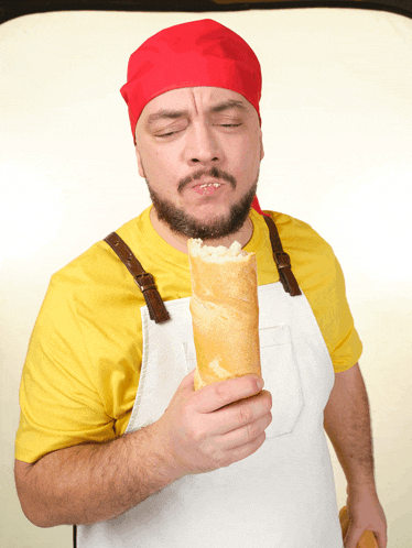 a man wearing a yellow shirt and an apron is eating a sandwich with his eyes closed