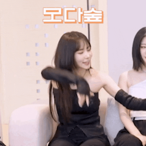 two women are sitting on a couch and one of them is wearing a black top and black gloves .