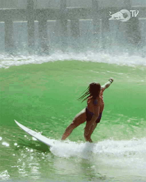 a woman is riding a wave on a surfboard with a red bull logo behind her