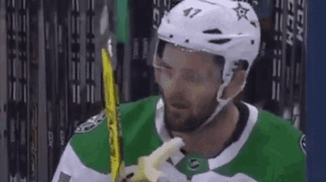 a hockey player is eating a banana while wearing a white helmet .