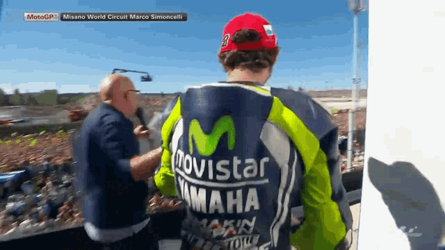 a man wearing a movistar yamaha jacket stands in front of a crowd of people