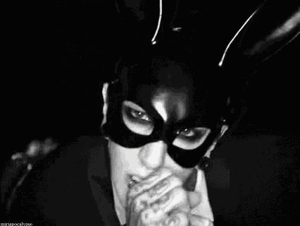 a woman wearing a cat mask is smoking a cigarette in a black and white photo .