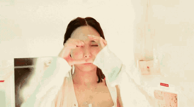a woman is making a heart shape with her hands on her face .