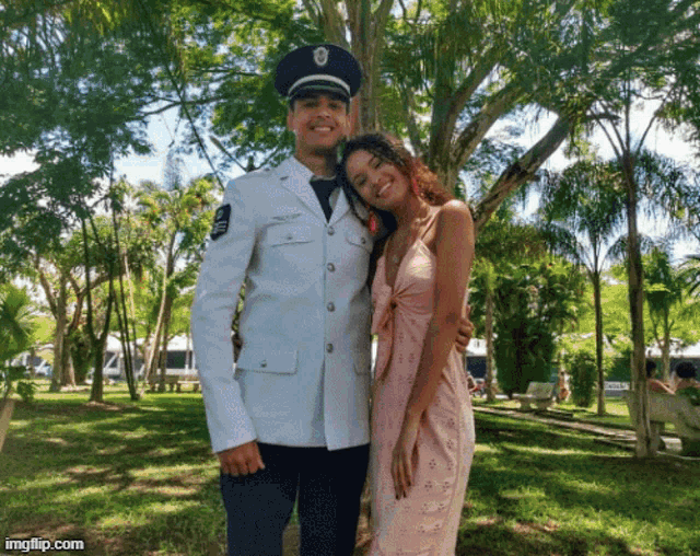 a man in a military uniform stands next to a woman in a pink dress in a park