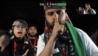 a man with a green scarf around his neck is holding his finger to his mouth