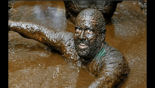 a man covered in mud is swimming in a muddy pool