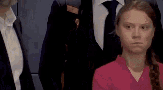 a woman in a pink shirt is standing in front of a group of people in suits and ties .