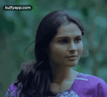a woman in a purple dress is standing in the woods looking at something .