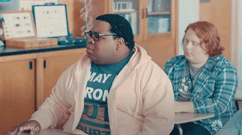 a man in a pink hoodie is sitting at a desk with another man .