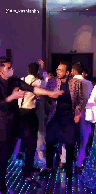 a group of people are dancing in a room with an exit sign in the background