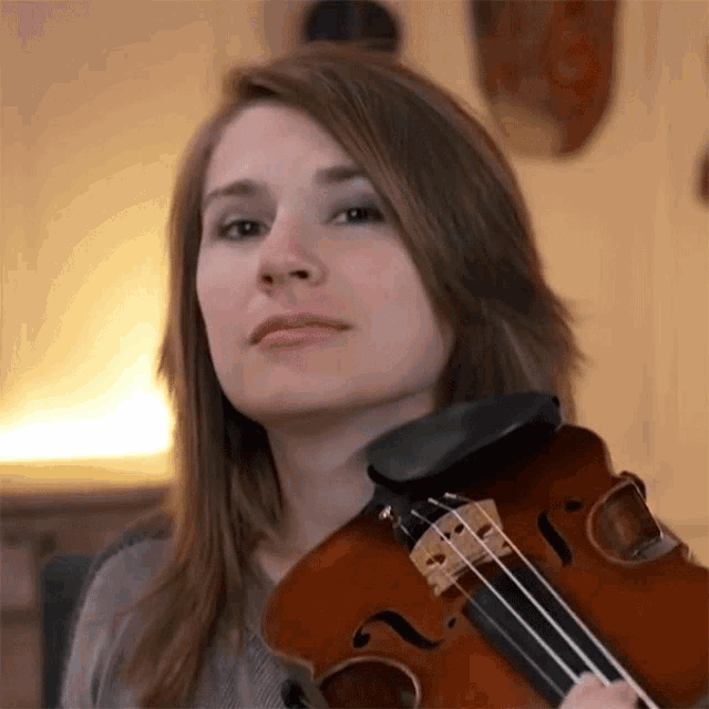 a woman playing a violin with a gray shirt on