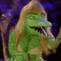 a green crocodile with blonde hair is sitting in a chair with its mouth open .