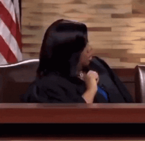 a woman in a judge 's robe is sitting in a courtroom holding a microphone .