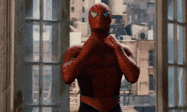 a man in a spiderman costume stands in front of a window with a city in the background
