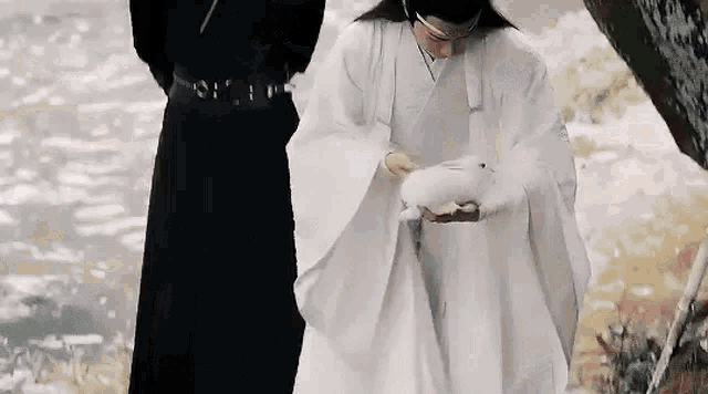 a man in a white robe is holding a small white rabbit in his hand .