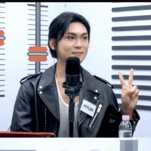 a man wearing a leather jacket with hyun written on it giving a peace sign