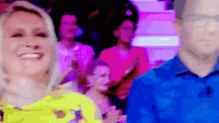 a woman in a yellow shirt is smiling in front of a crowd of people