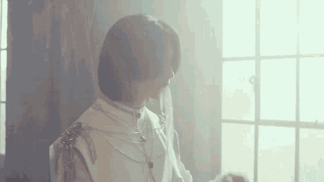 a woman in a white dress is standing in front of a window in a dark room .