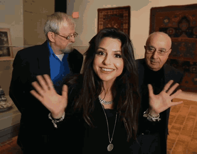 a woman in a black dress is smiling with two men behind her and an exit sign in the background