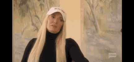 a woman wearing a hat and a black turtleneck is standing in front of a painting .