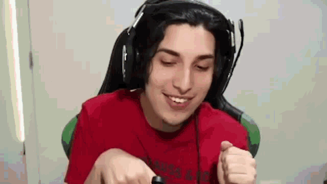 a young man wearing headphones and a red shirt is sitting in a chair and smiling .