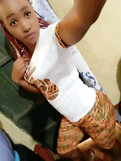 a girl taking a selfie with a white shirt with a snake on it and orange shorts