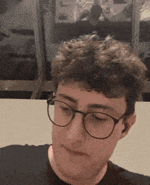 a man wearing glasses and a black shirt looks down at something