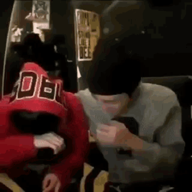 a couple of people are sitting next to each other in a room . one of the people is wearing a red hoodie .
