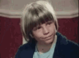 a young boy with blonde hair is sitting in a chair and making a face .