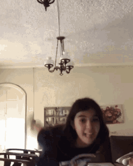 a woman is sitting at a table with a chandelier hanging from the ceiling