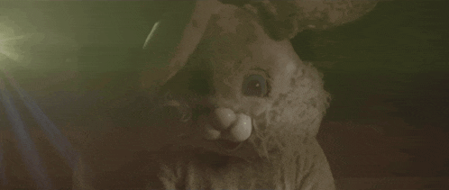 a creepy stuffed bunny rabbit is looking at the camera in a dark room .