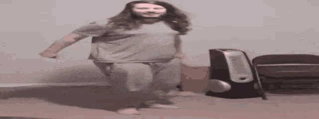 a man with long hair is dancing in a living room next to a speaker .