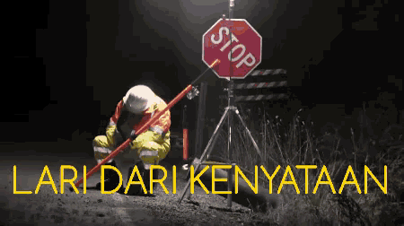 a man kneeling in front of a stop sign with lari dari kenyataan written below it