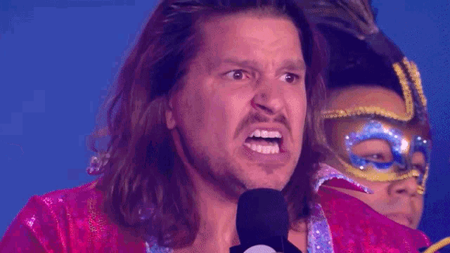 a man with long hair and a mask is talking into a microphone and says a stupid .