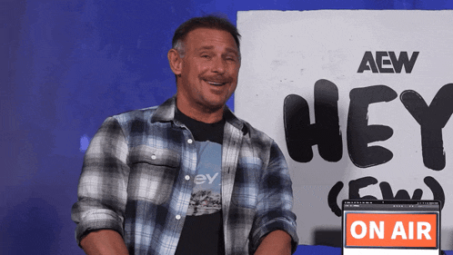 a man in a plaid shirt is smiling in front of a sign that says hey